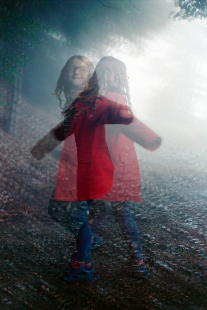 double exposure of a little girl with a red jacket, as she swirls around in the forest