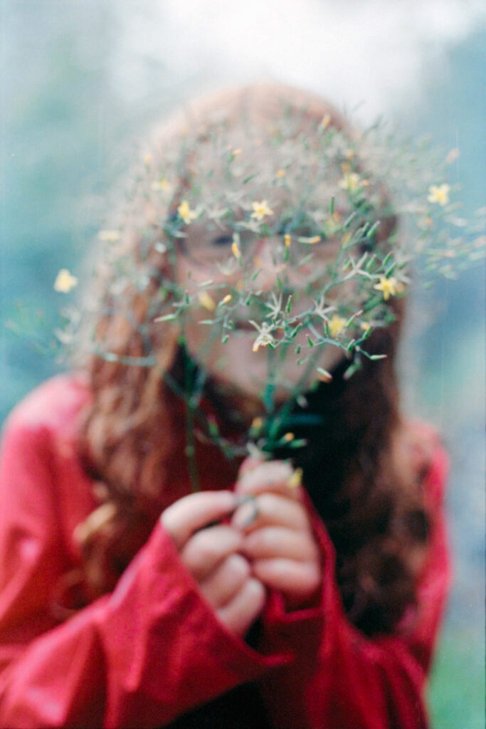 photograph of a little girl playfully hiding her face behind branches of tiny mountain flowers