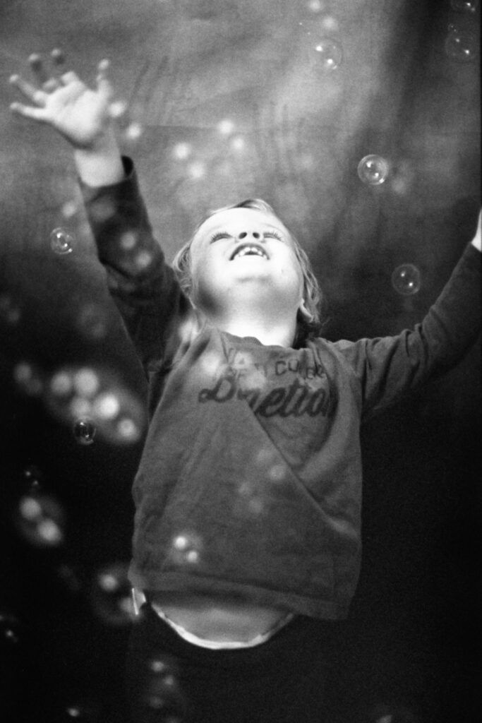 Monochrome photograph of a toddler boy trying to catch bubbles in a studio against a backdrop
