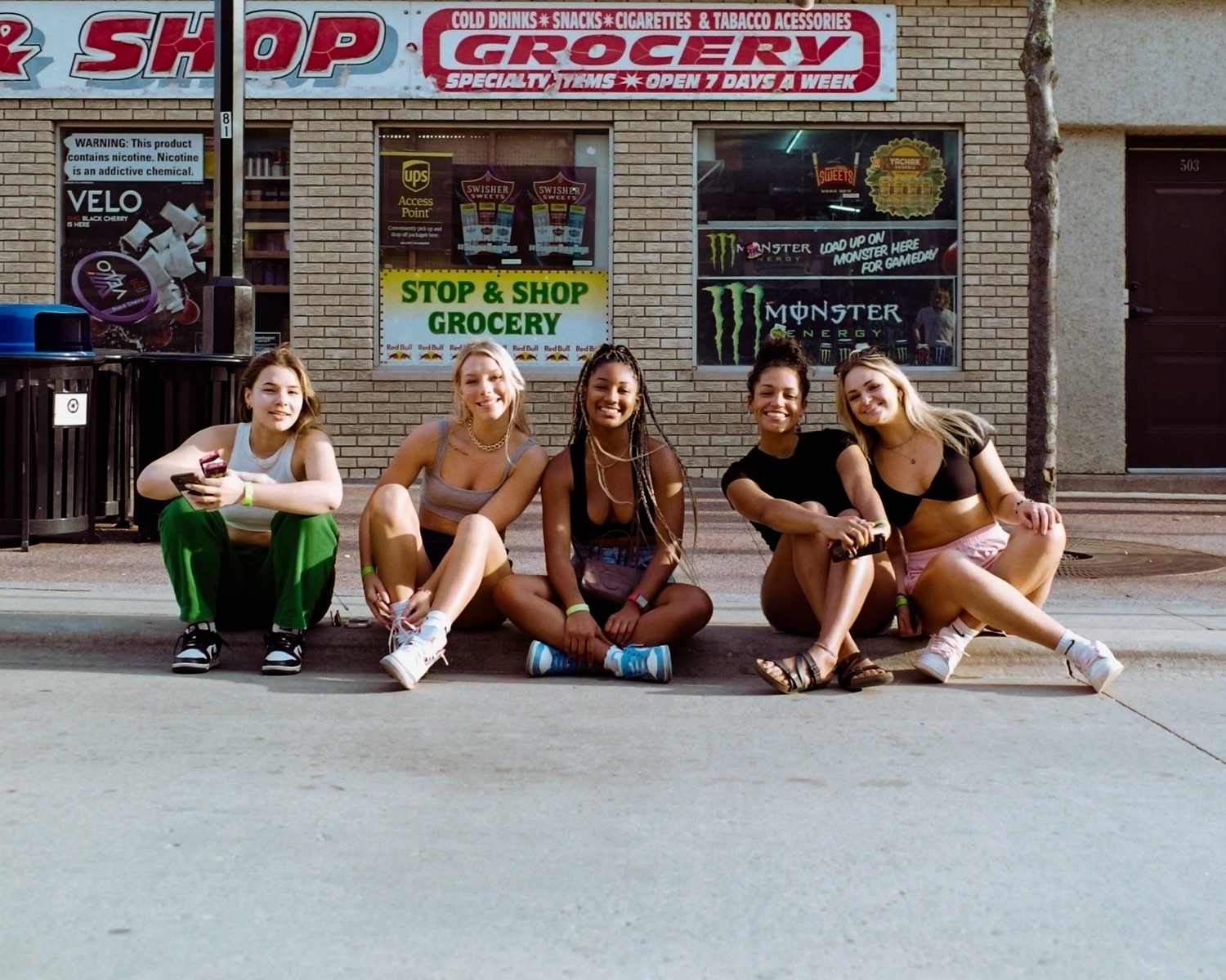 Group picture of a group of young girl friends with every skin color, sitting on the sidewalk on a warm spring day on State Street, in Madison, Wisconsin