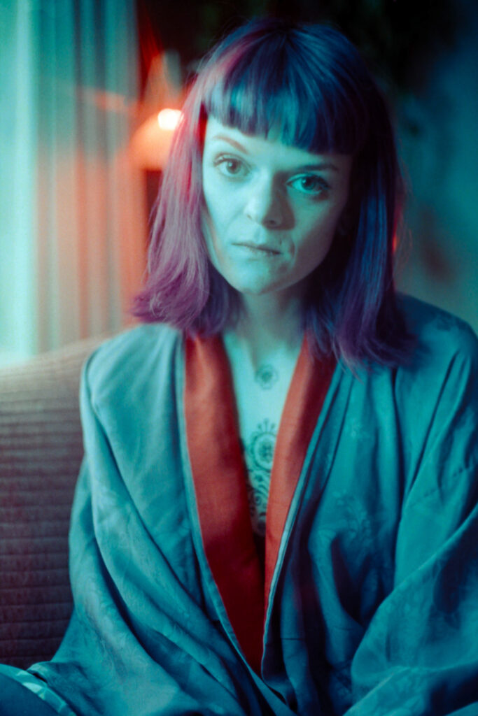 Portrait of a young woman with purple hair, wearing a Kimono in blue light with a start shaped red light shining behind her head