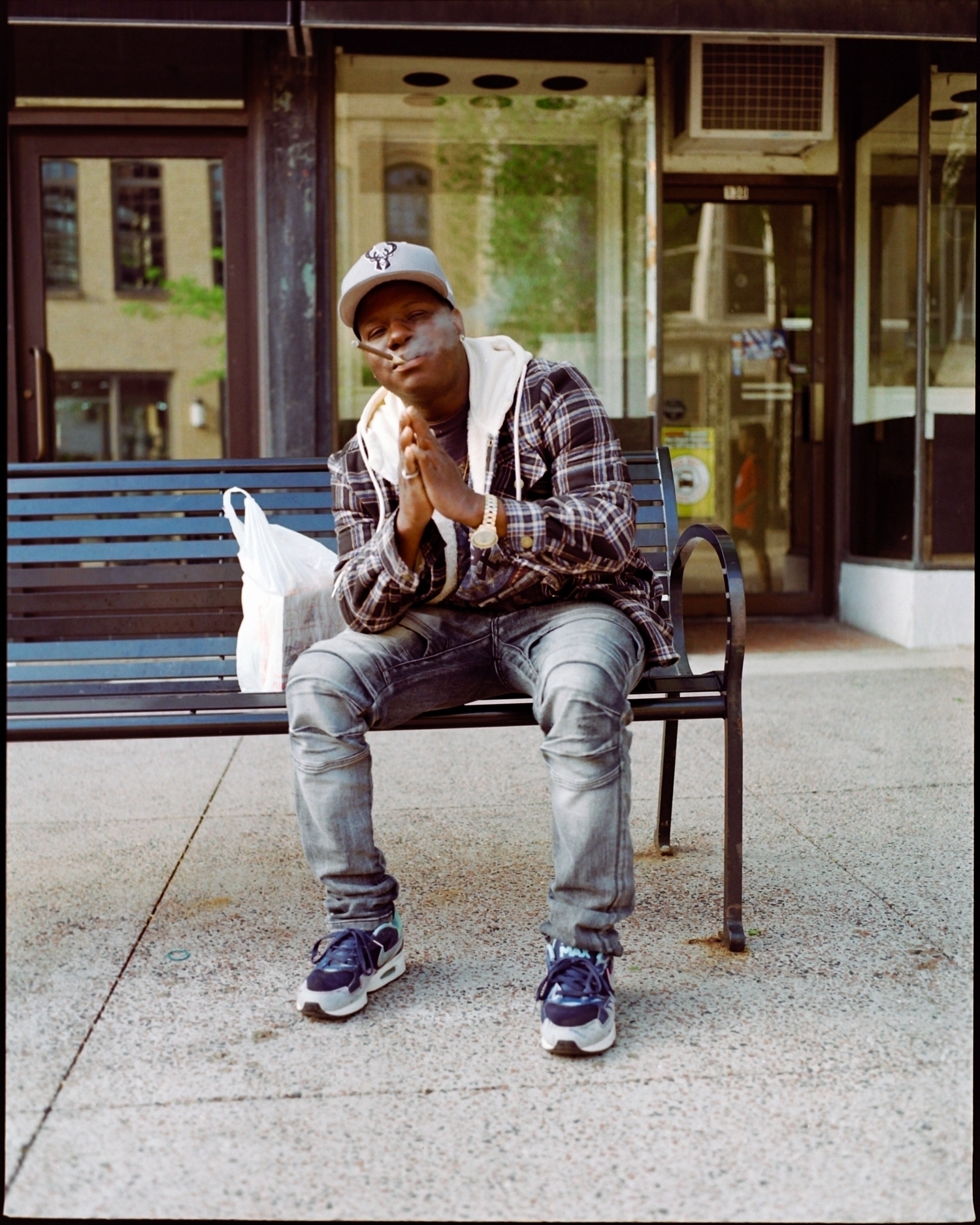 Portrait of a black man with a baseball cap, smoking a ccigarillo and holding his hands like in a prayer, with a demeanor not unlike Thomas O'Malley.