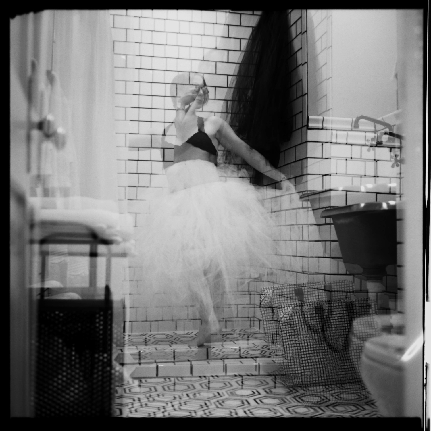 Double-exposure black-and-white portrait of a woman swirling in a white tutu in a bathroom
