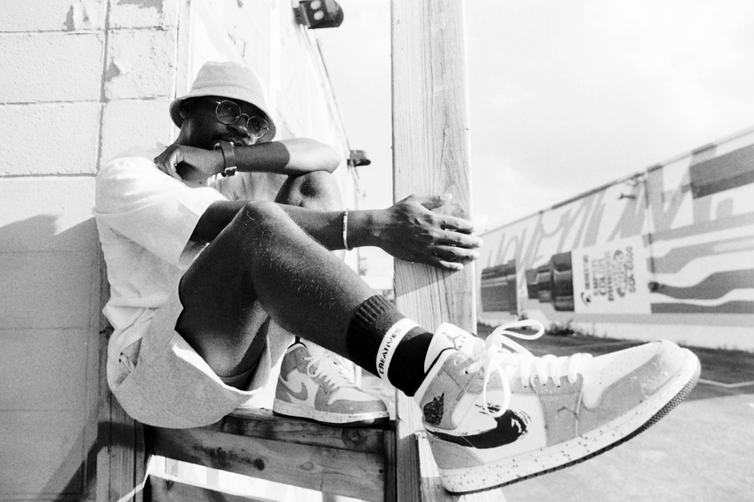 wide-angle Black-and-white portrait of a young hip-hop artist, a black man wearing a pair of Nike sneakers.