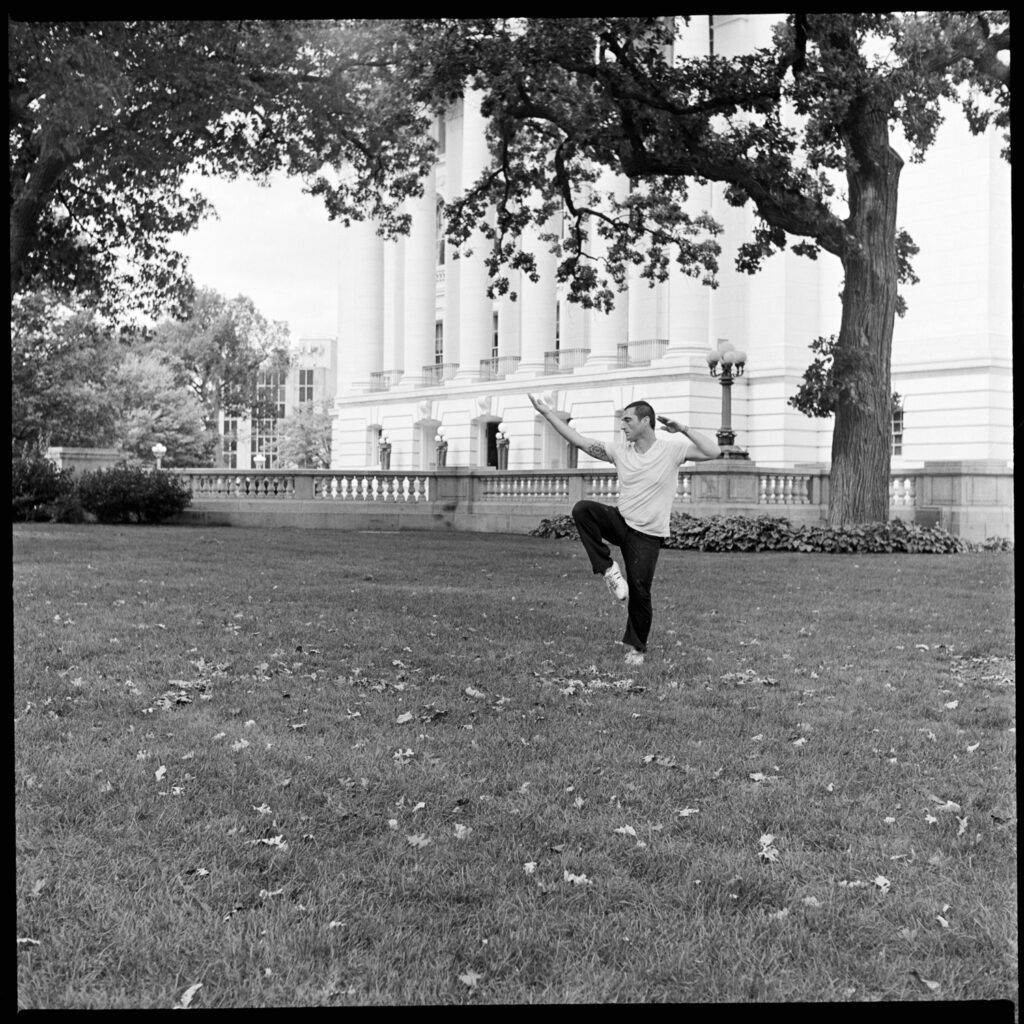 Black-and-white photograph of a man practicing Qi-Cong on the grass by the side of Wisconsin's State Capitol in Madison, Wisconsin