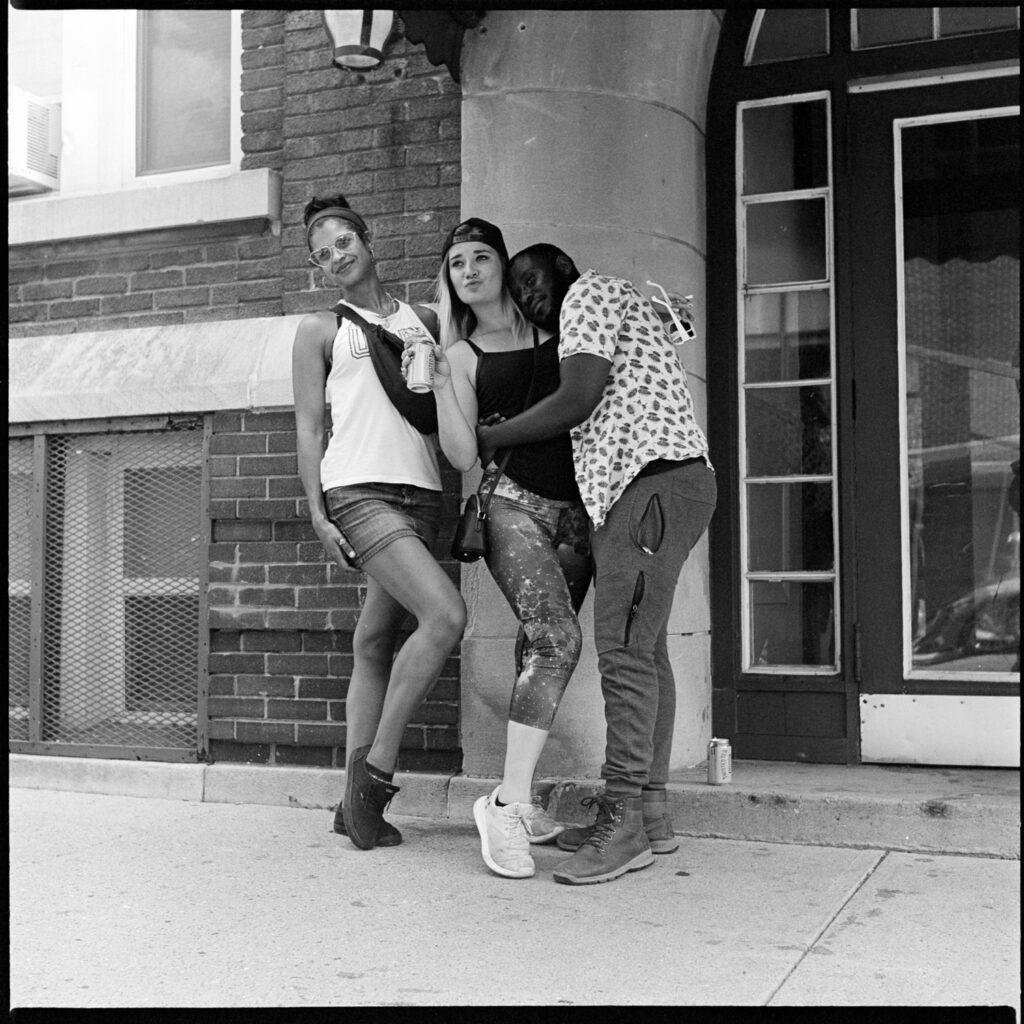 Black-and-white photograph of three friends posing in a hug for another photographer next to a residential building door