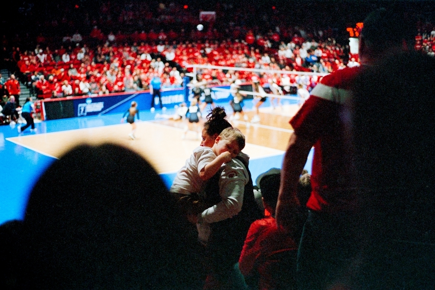 Photograph of a child who fell asleep in his mother's arms at the end of a University of Wisconsin, Madison Volleyball game