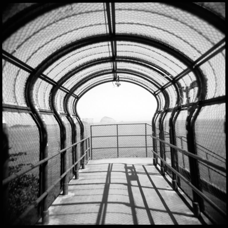 Black-and-white photograph of a pedestrian bridge covered in chickenwire in the shape on a keyhole