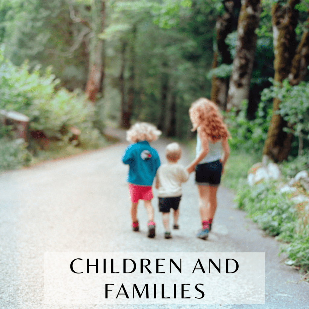 Dreamy film photograph of a group of three children holding hands while walking down a paved trail in a mountain forest