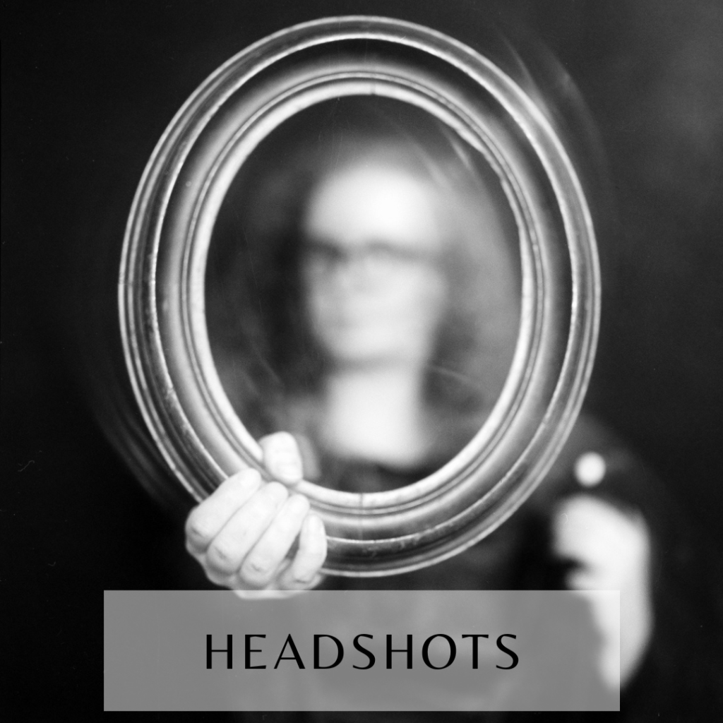 Black-and-white large format photograph of a woman behind an oval frame she's holding and that's in focus, with her face blurred as if to ask who she is