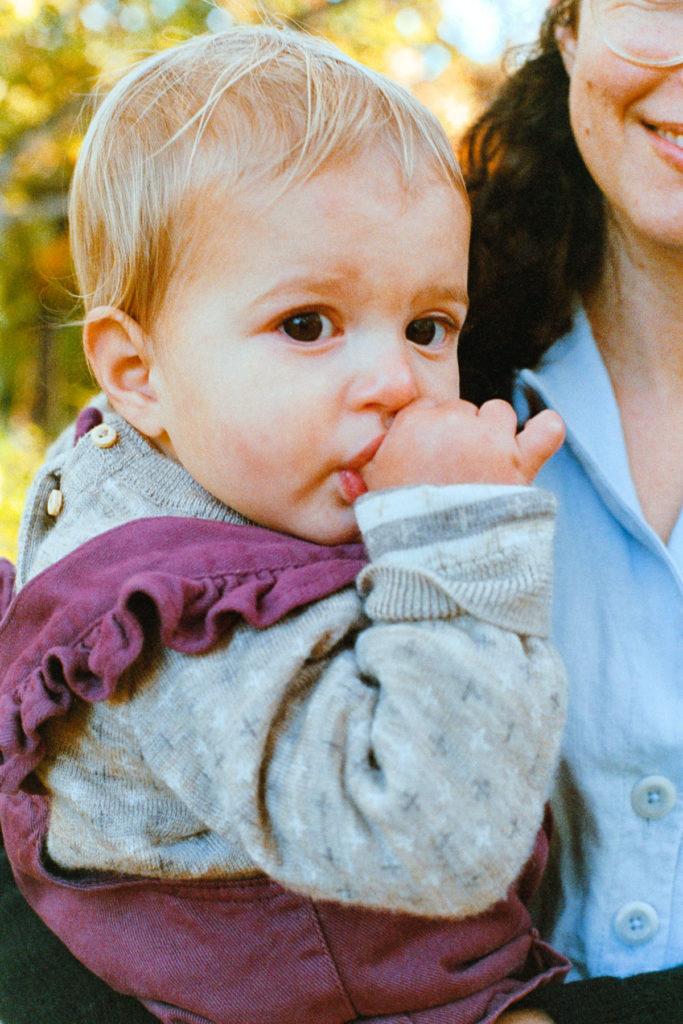 Portrait of a one-year old blonde girl sucking on her thumb in her mother's arms