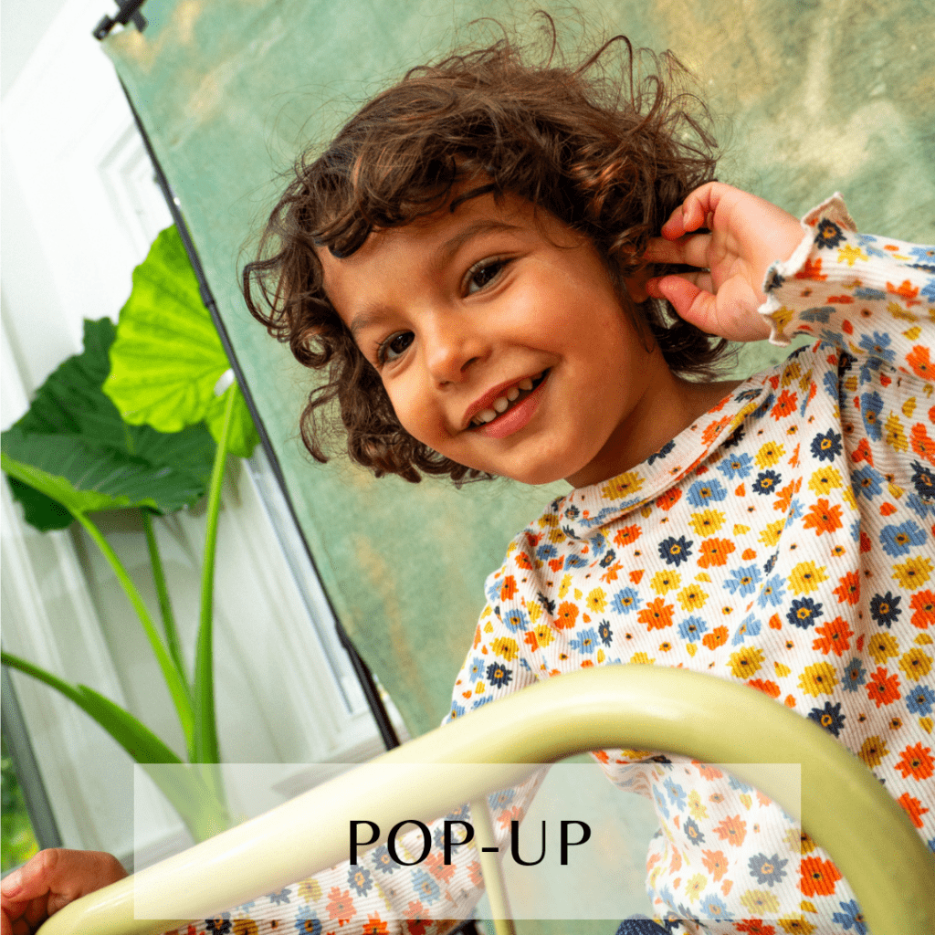 Photograph of a little girl wearing a floral tshirt, in front of a green and gold hand-painted backdrop with the setup apparent