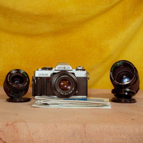 Product photo of the camera Minolta XGM with the two extra lenses and some documentation
