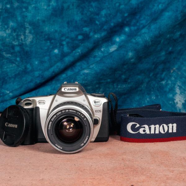 Product photo of the Canon Rebel2000 camera with camera strap visible, showing the Canon logo