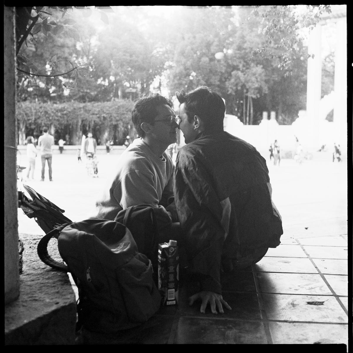 analog black-and-white street photograph of a gay couple making out in Parque México on a Saturday afternoon