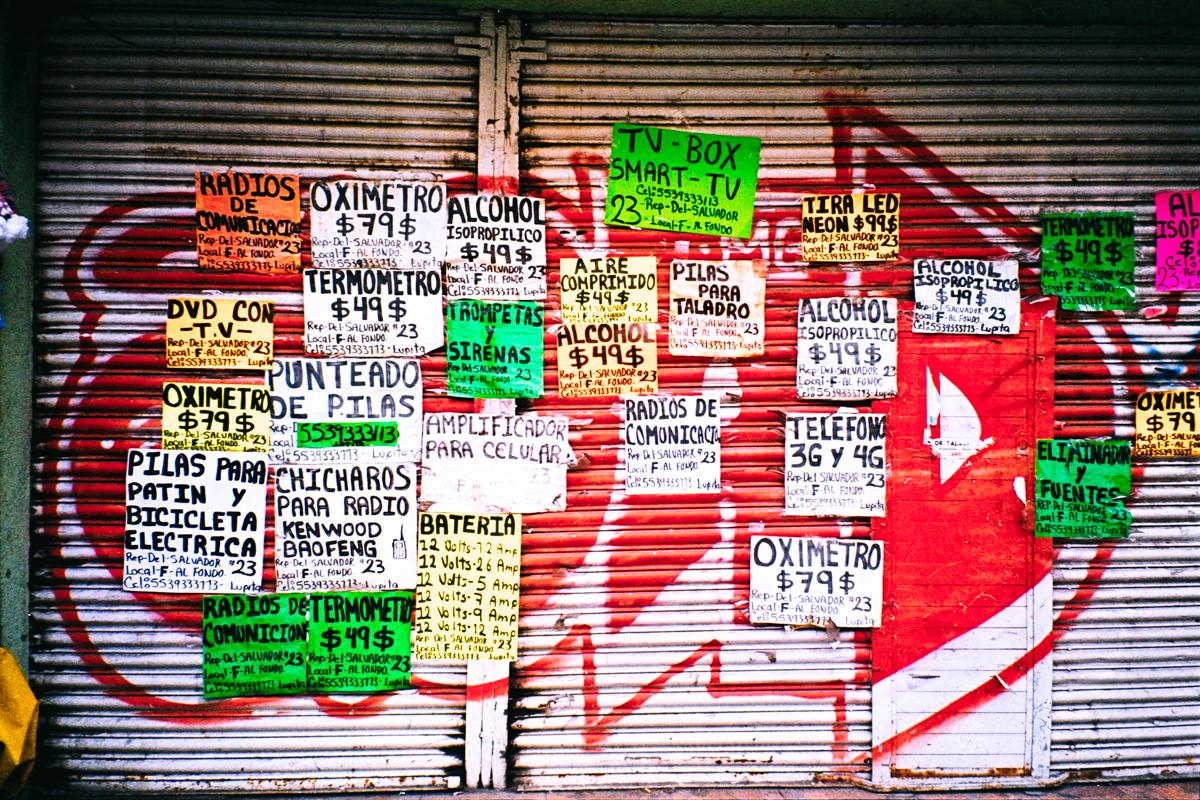 Photograph of lowered shop shutters covered in hand-written product adverts