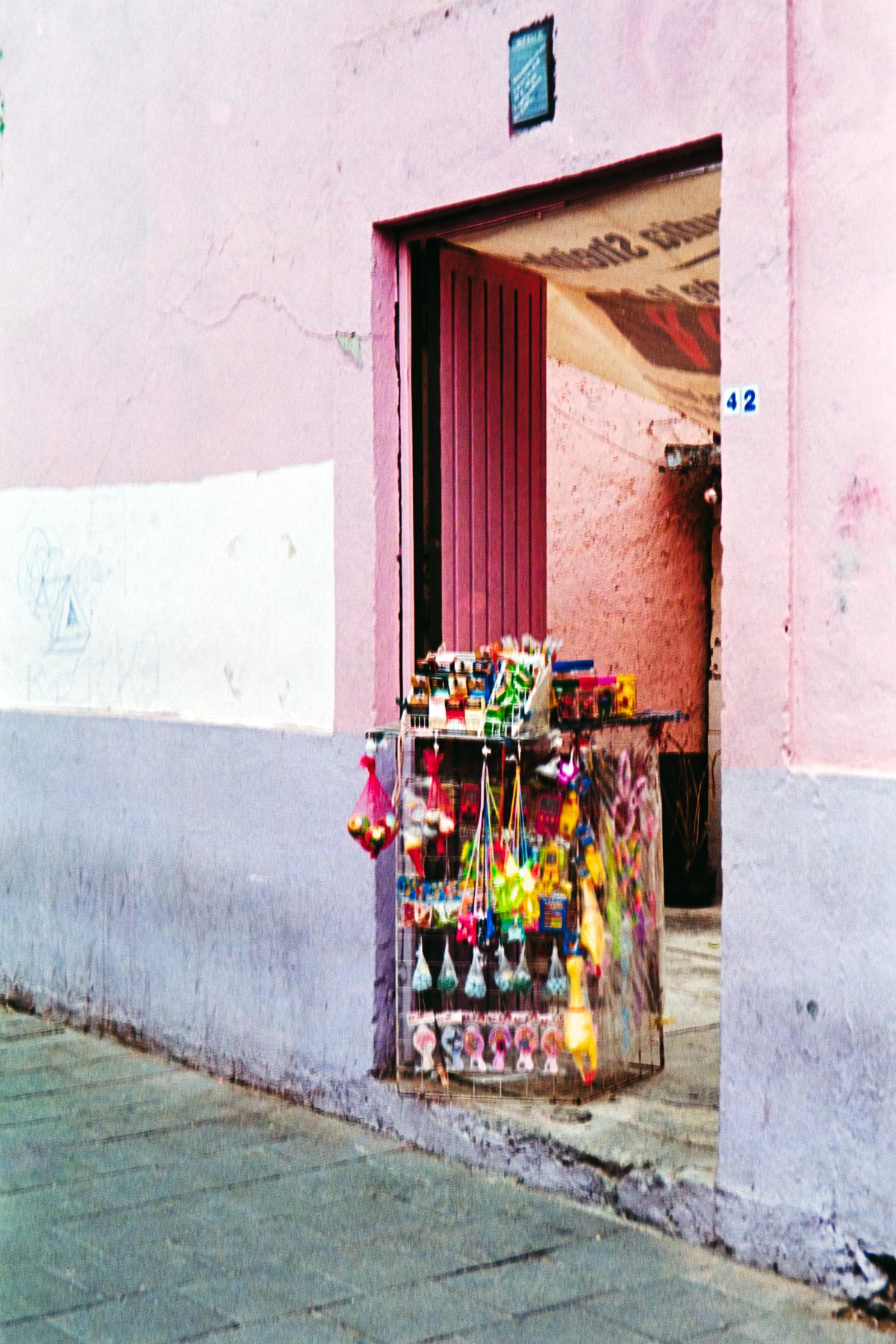 photograph of a door in a pink wall in Mexico city, with unattended candy cart standing in the frame