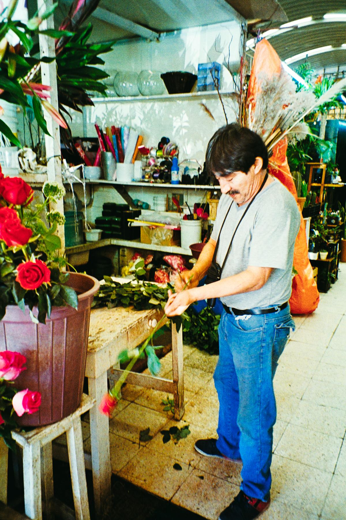 analog street photograph of a flower vendor preparing red roses in a market in Mexico City