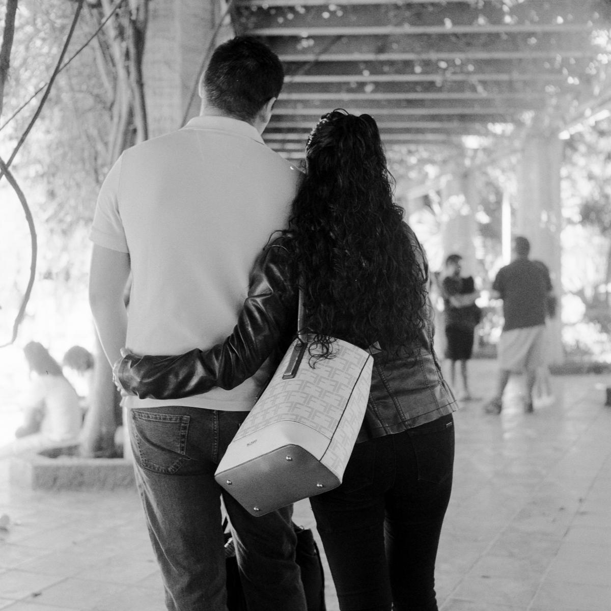 analog black-and-white street photograph of a couple hugging, seen from behind, in Parque México on a Saturday afternoon