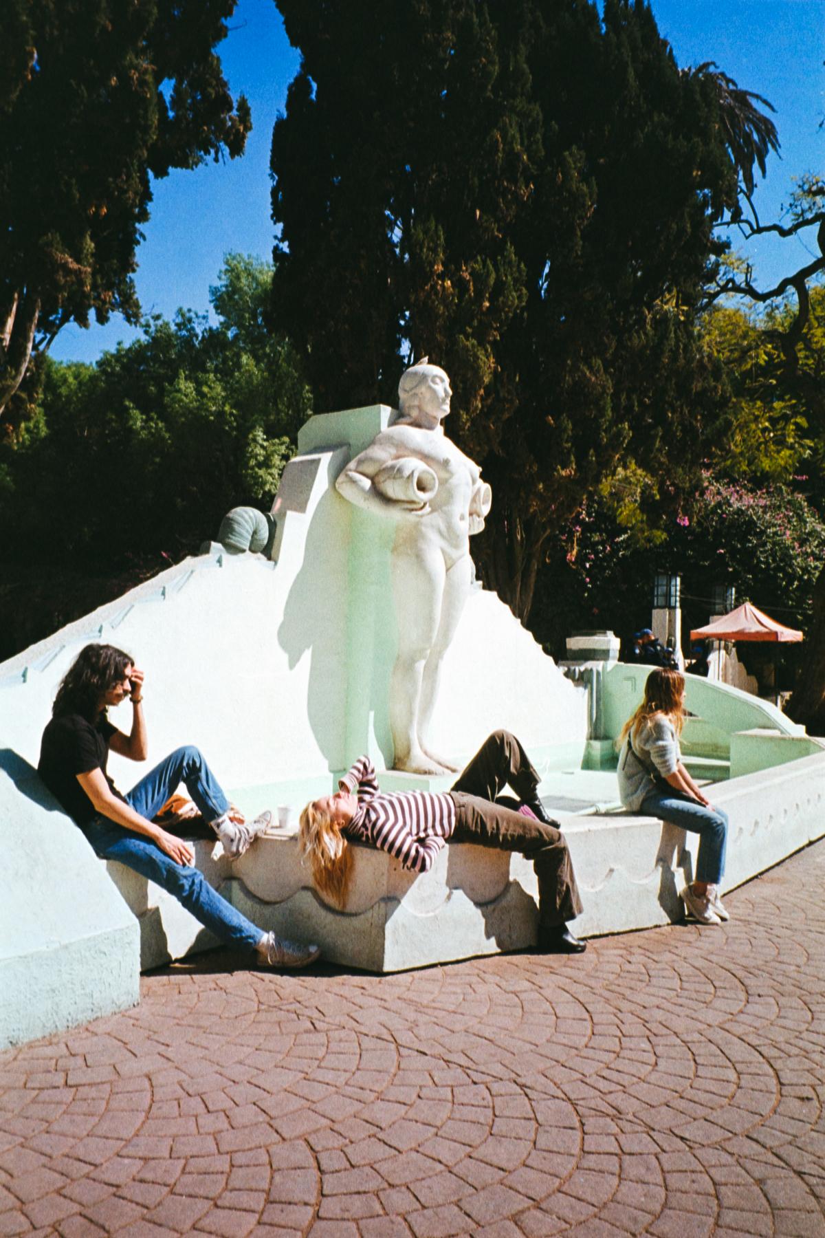 analog street photograph of young people napping under a statue in Parque México on a Saturday afternoon