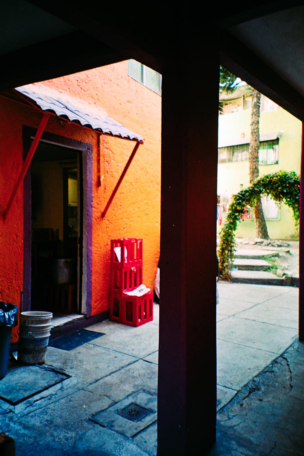photograph of a building interior, with orange wall, red crates, and greenery in the background