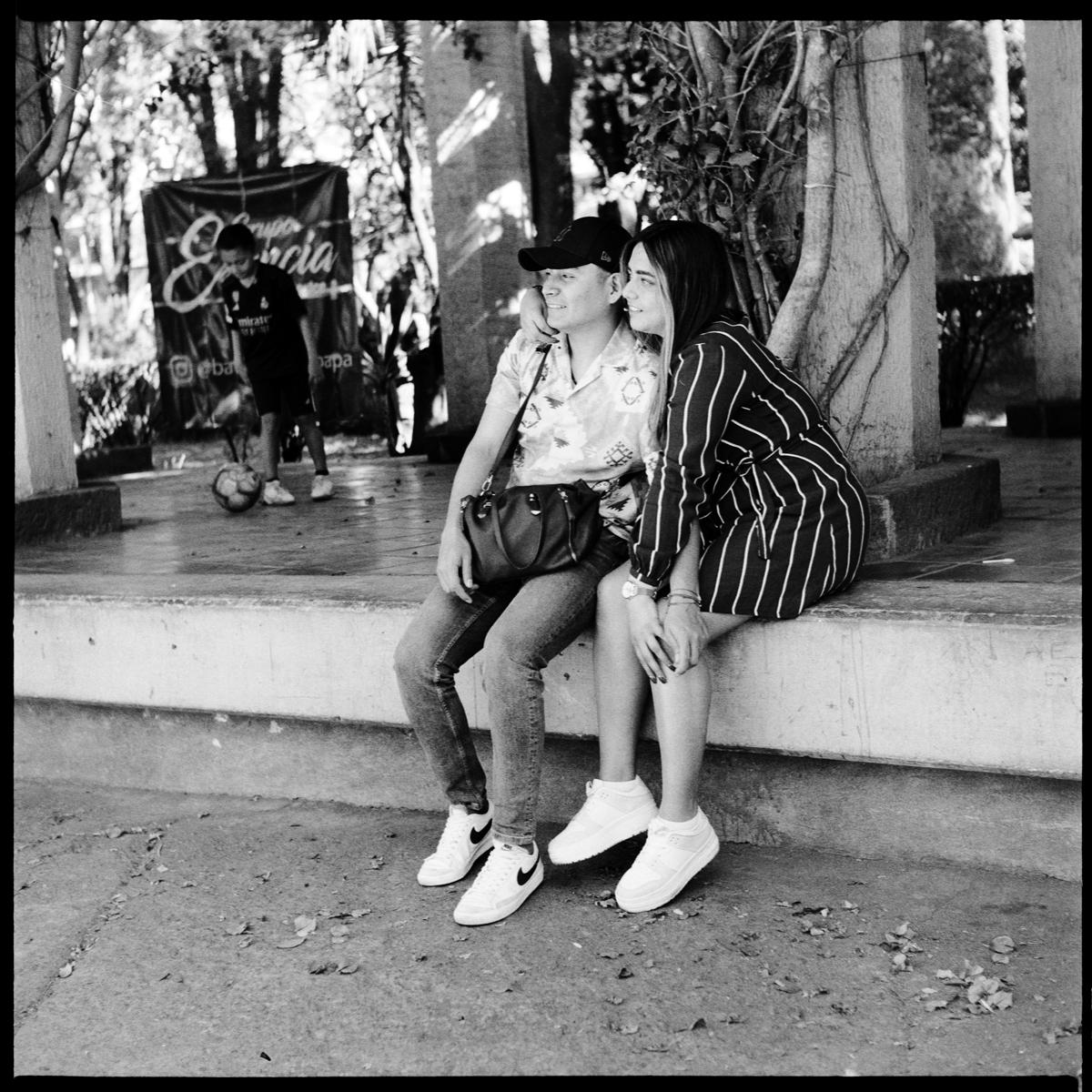 analog black-and-white street photograph of a couple hugging, sitting on a wall, in Parque México on a Saturday afternoon
