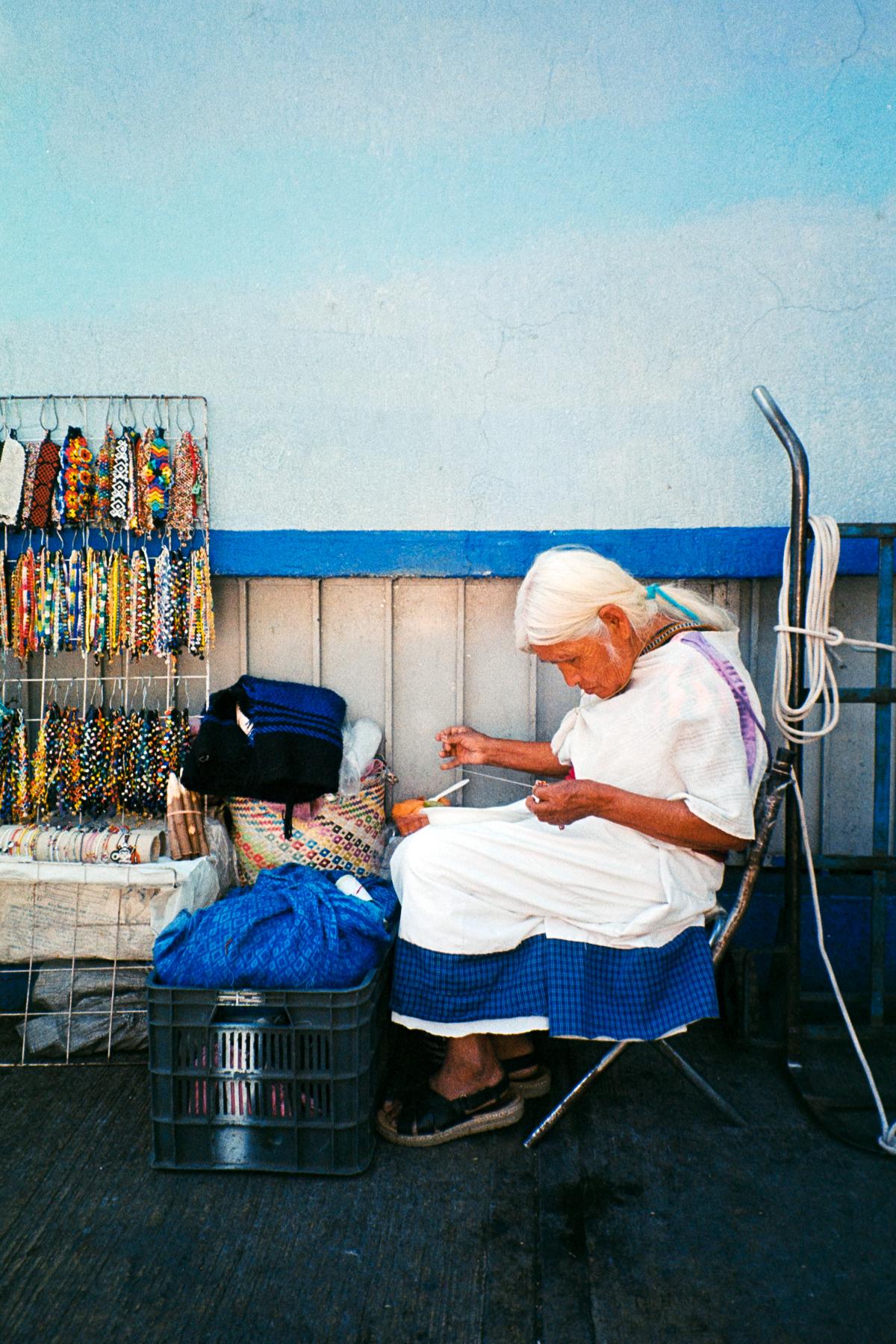 analog street photograph of a elderly lady making beadwork on her street vending stand in Mexico City